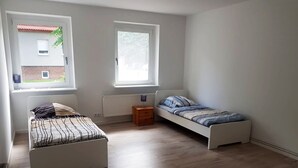Quarto com duas camas, um radiador e duas janelas.
