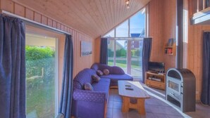 A cozy room with a large window, a sofa, a small table, and a wood-burning stove.