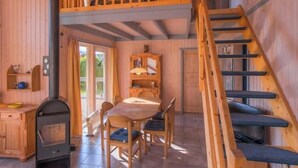 Interior de una cabaña de madera con comedor, habitación en un entrepiso y una escalera.