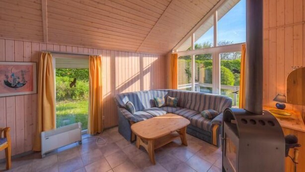 Una habitación acogedora con techo de madera, un ventanal grande, un sofá, una mesa y un estufa de leña.