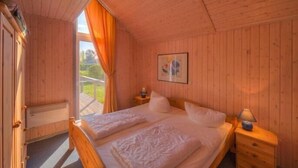 Un dormitorio con paneles de madera, una cama, dos mesitas de noche y un ventanal con cortinas.