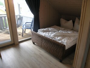 Relax in this serene bedroom with a large bed and a wicker chair by the window, offering a view of the outdoor area.