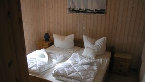 A wooden-paneled room with a bed, pillows, a nightstand, and a lamp. - Seeschwalbe Classic 63 - Spacious vacation home with its own sauna (Rechlin-Nord)