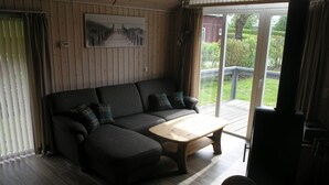 A cozy room with a dark-colored sofa, a wooden coffee table, and a painting of a pathway on the wall. - Seeschwalbe Classic 63 - Spacious vacation home with its own sauna (Rechlin-Nord)