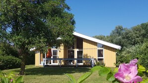 A yellow building with a balcony, surrounded by greenery and a tree.