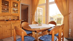 A wooden dining area with a table and chairs, a cabinet with glass doors, and a window with curtains.