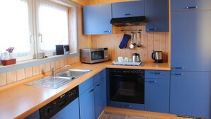 A compact kitchen with wooden cabinets, a microwave, a dishwasher, and a window with curtains.