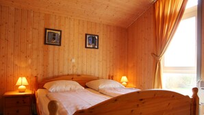 A wooden-paneled room with two beds, two bedside lamps, and a window with curtains.