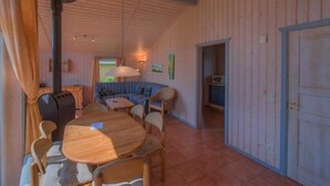 A cozy room with a wooden ceiling, a round dining table with chairs, a sofa, and a door leading to another room.
