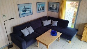Un sofá de color oscuro con dos almohadas, una mesa de centro de madera con un objeto azul encima, y tres cuadros enmarcados en la pared.