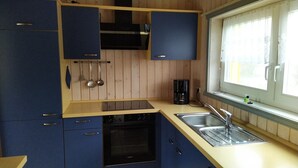 Una cocina con armarios azules, un lavavajillas Siemens, una cafetera y una ventana con cortinas.