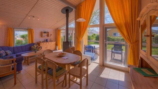 Una sala de estar acogedora con sofá, mesa de comedor y sillas, chimenea y ventanas grandes con cortinas.