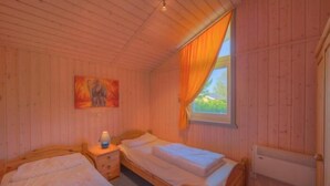 Una habitación con dos camas de madera, una mesita de noche con lámpara, un cuadro en la pared y una ventana con cortinas.