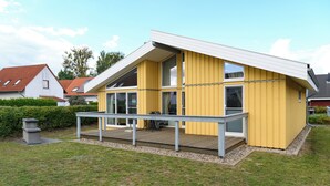 Une maison jaune moderne dotée d’un balcon, d’une terrasse en bois et d’un petit jardin.