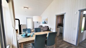 Un espace de repas moderne avec une table et des chaises en bois, une lampe et une vue sur la cuisine et le salon.