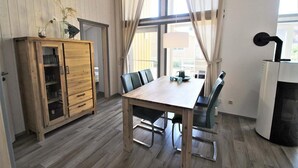 Un coin repas avec une table et des chaises en bois, un meuble avec des portes en verre et une grande fenêtre avec des rideaux.
