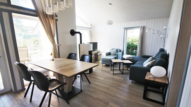 Una sala de estar moderna con una mesa de comedor de madera, sillas negras, un sofá y un televisor.