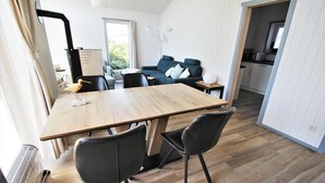 Una habitación moderna con una mesa de comedor de madera, dos sillas negras, un sofá gris con cojines y una cocina visible a través de un umbral abierto.