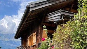 Ein rustikales Holzhaus mit Balkon, umgeben von üppigem Grün und leuchtenden Blumen.