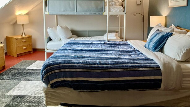 Una cama individual con ropa de cama a rayas azules, una mesita de noche con lámpara, y un cuadro en la pared.