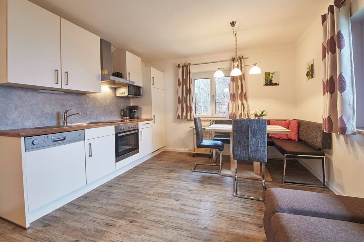 Eine moderne Küche mit weißen Schränken, einem Geschirrspüler und einem Essbereich mit Tisch und Stühlen.