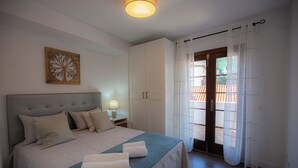 Un dormitorio ordenado con una cama, una mesita de noche, una lámpara y una puerta que da a un balcón.