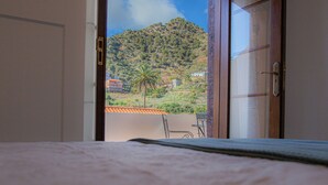 Una habitación con una cama y vistas a un balcón con mesa y sillas, una montaña y una palmera.