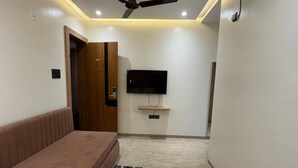 A bedroom with a bed, a sofa, a ceiling fan, a TV, and an air conditioning unit. - Hotel Manoranjan Enclave (Dindori)