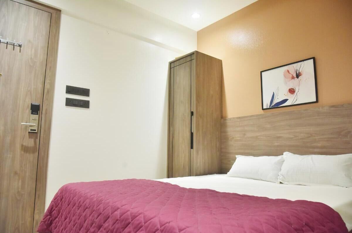 A hotel room with a bed, a wardrobe, and a painting on the wall.