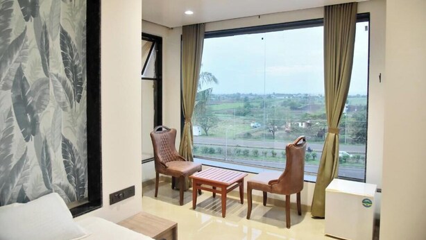 A hotel room with a large window, two chairs, a small table, and a bed. - Hotel Manoranjan Enclave (Dindori)