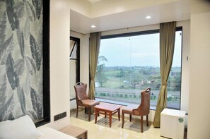A hotel room with a large window, two chairs, a small table, and a bed.