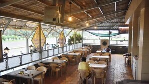A restaurant with outdoor seating, tables, and chairs arranged under a covered area with a view of the street. - Hotel Manoranjan Enclave (Dindori)