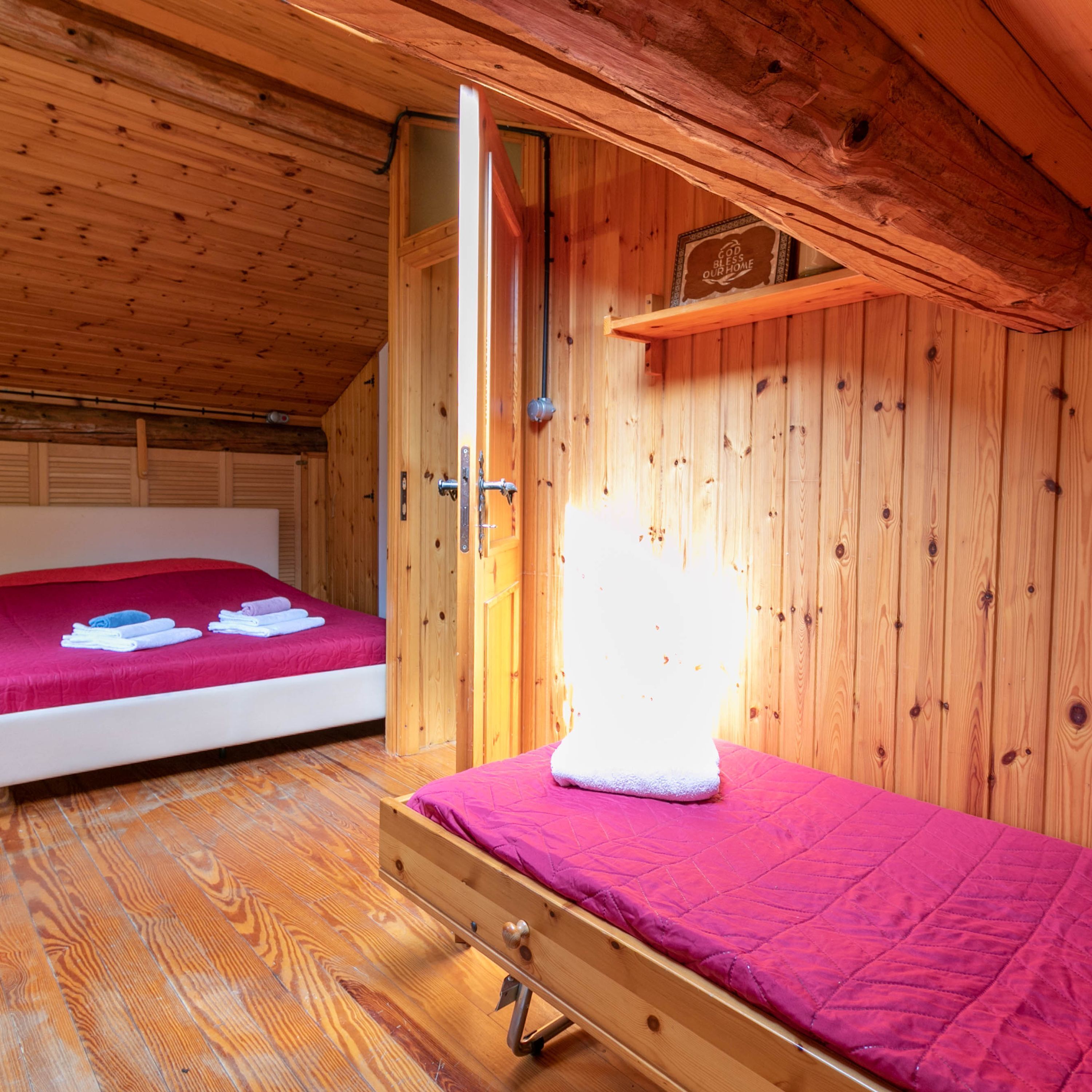 A wooden room with a bed, a wooden shelf, and a door.