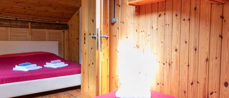 A wooden room with a bed, a wooden shelf, and a door.