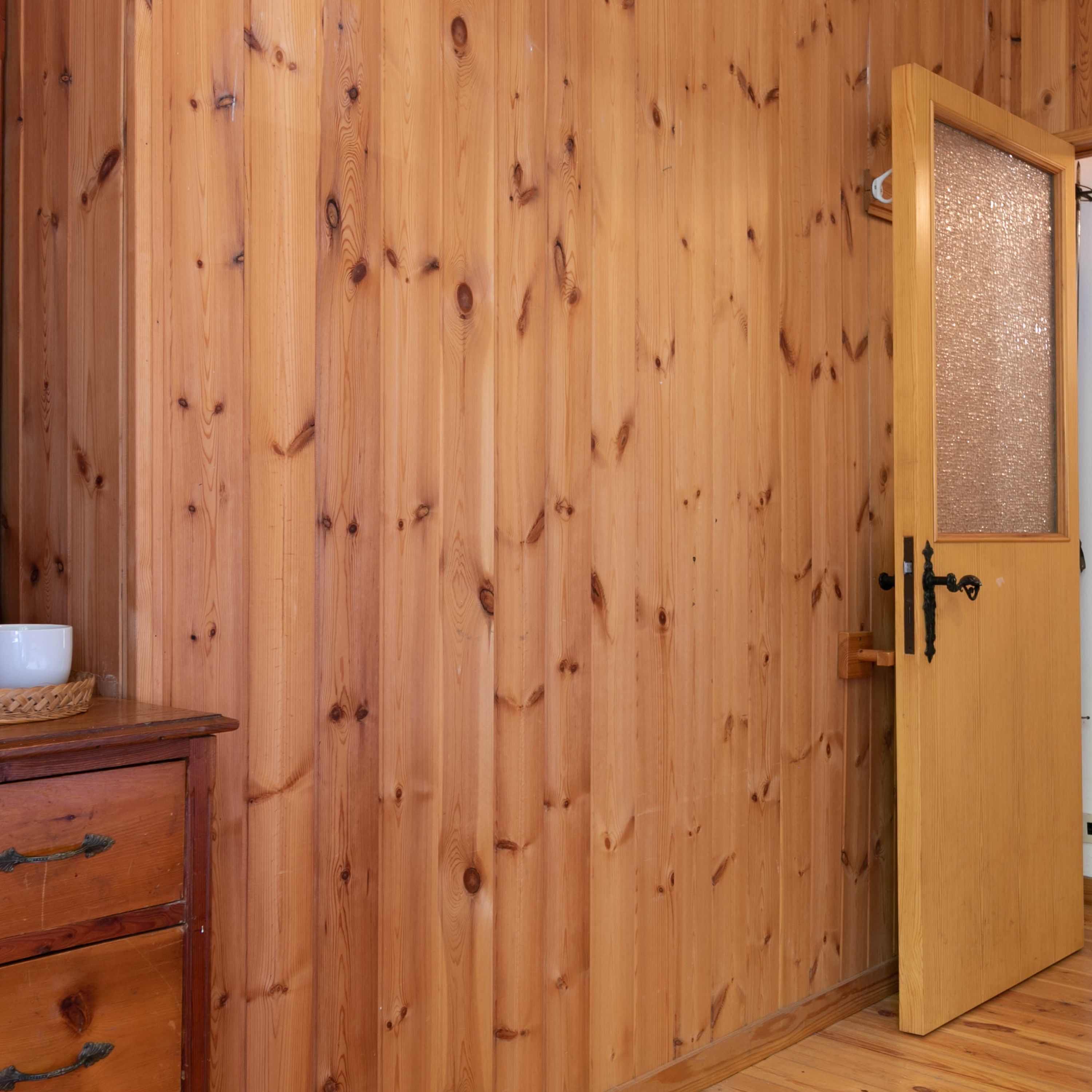 Una habitación de madera con una puerta, un pequeño aparador de madera y una cesta tejida sobre el aparador.