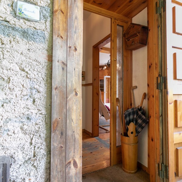 A rustic wooden interior with a stone wall, wooden door, and a small wooden bucket with a plaid bag.