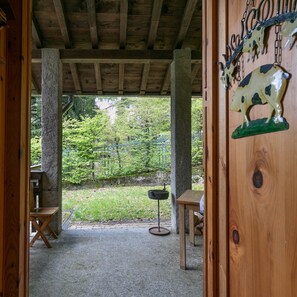 A rustic wooden structure with a concrete floor, a metal table, and a metal chair.