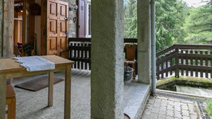 Ein rustikaler Holztisch mit Unterlage, eine hölzerne Bank und eine Steinwand mit Holztür und -fenster.