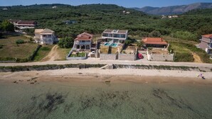 A coastal property with multiple houses, a swimming pool, and a beach in the foreground.