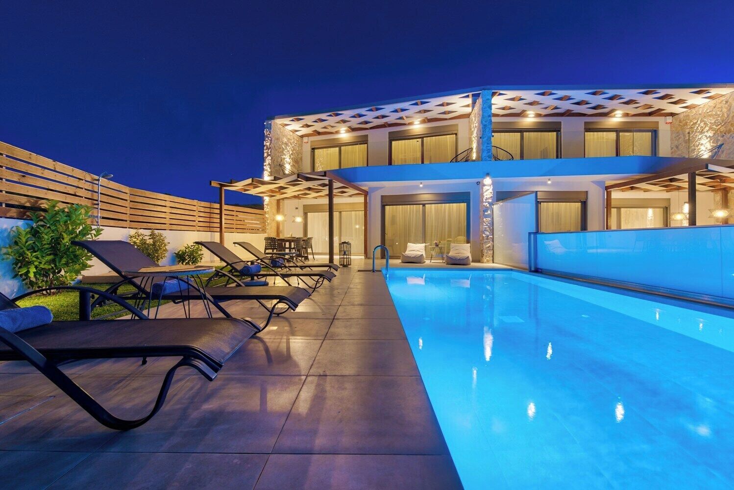En pool på taket med solstolar och en modern byggnad i bakgrunden.