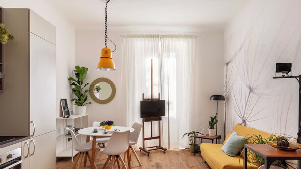 A modern living room with a yellow sofa, a dining table with chairs, a TV on a stand, and a kitchen area with cabinets and a stove. - Elegant apartment for 5, DUOMO in 10" by subway M3 (Milano)