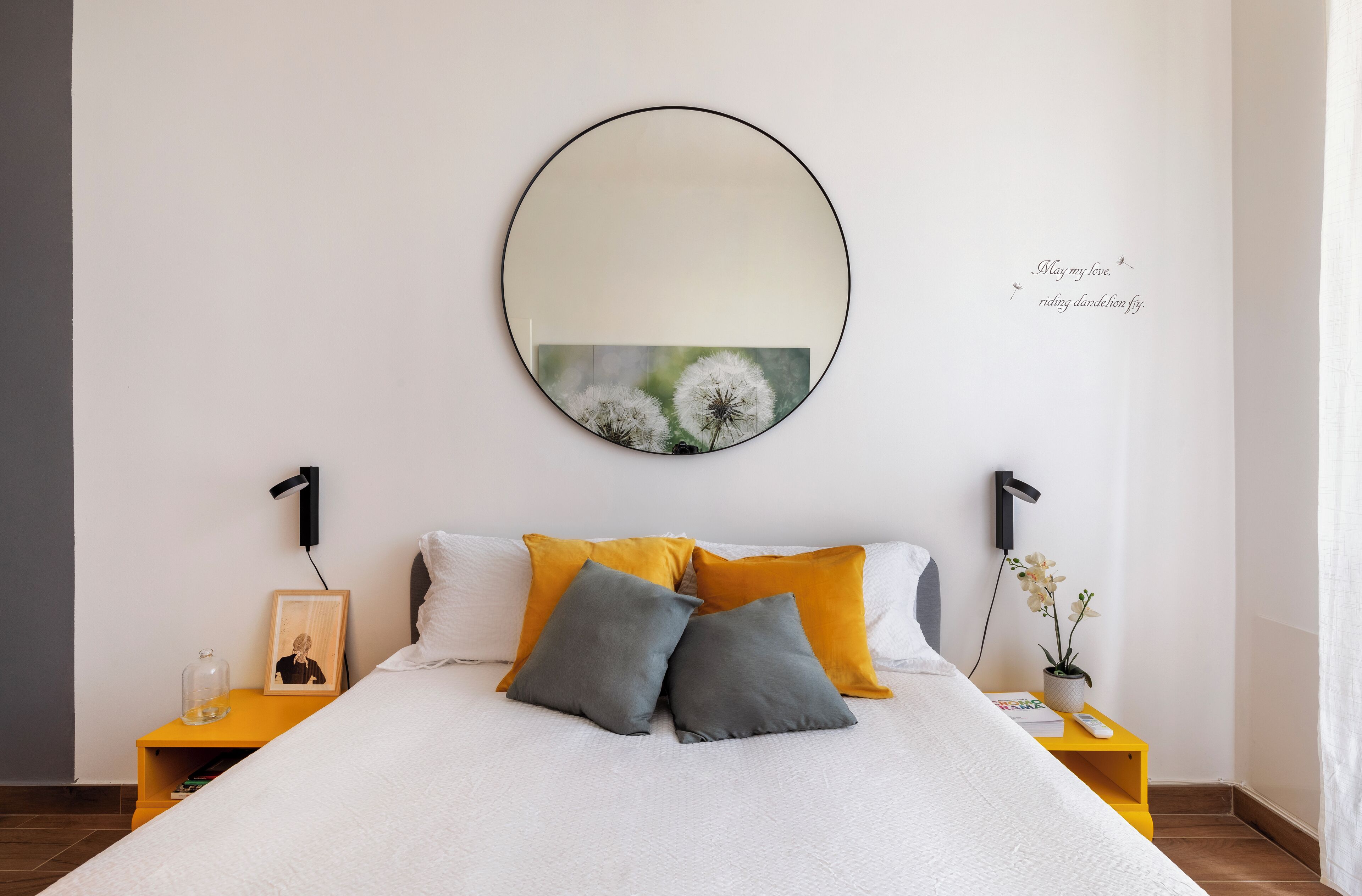 Un dormitorio ordenado con una cama grande, dos mesitas de noche, un espejo montado en la pared y una pequeña planta en maceta.