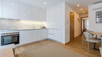 Una cocina moderna con armarios blancos, horno integrado y una zona comedor de madera con mesa y sillas.