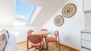 A modern living room with a skylight, a round wooden table, and four matching chairs. There are two decorative wall plates above the table. - Morais Soares 131 (Lisbon)