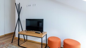 A modern room with a TV on a wooden table, a tripod, and two orange ottomans. - Morais Soares 131 (Lisbon)