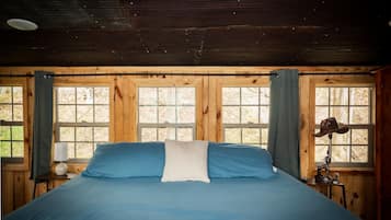 Ein Zimmer mit einem Bett, zwei Fenstern, einer Lampe und einem Hut auf einem Tisch.