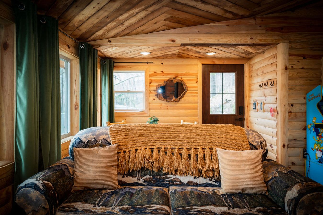A cozy cabin room with a bed, a wooden ceiling, and a window with curtains.