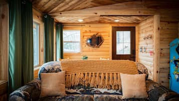 A cozy cabin room with a bed, a wooden ceiling, and a window with curtains.