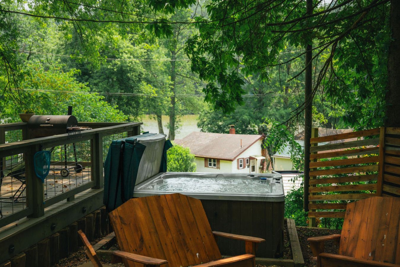 Un bain à remous sur une terrasse en bois, avec vue sur une maison et des arbres.