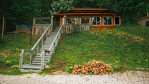 Een chalet met een houten gevel, een trap naar een terras en een stapel hout ervoor.